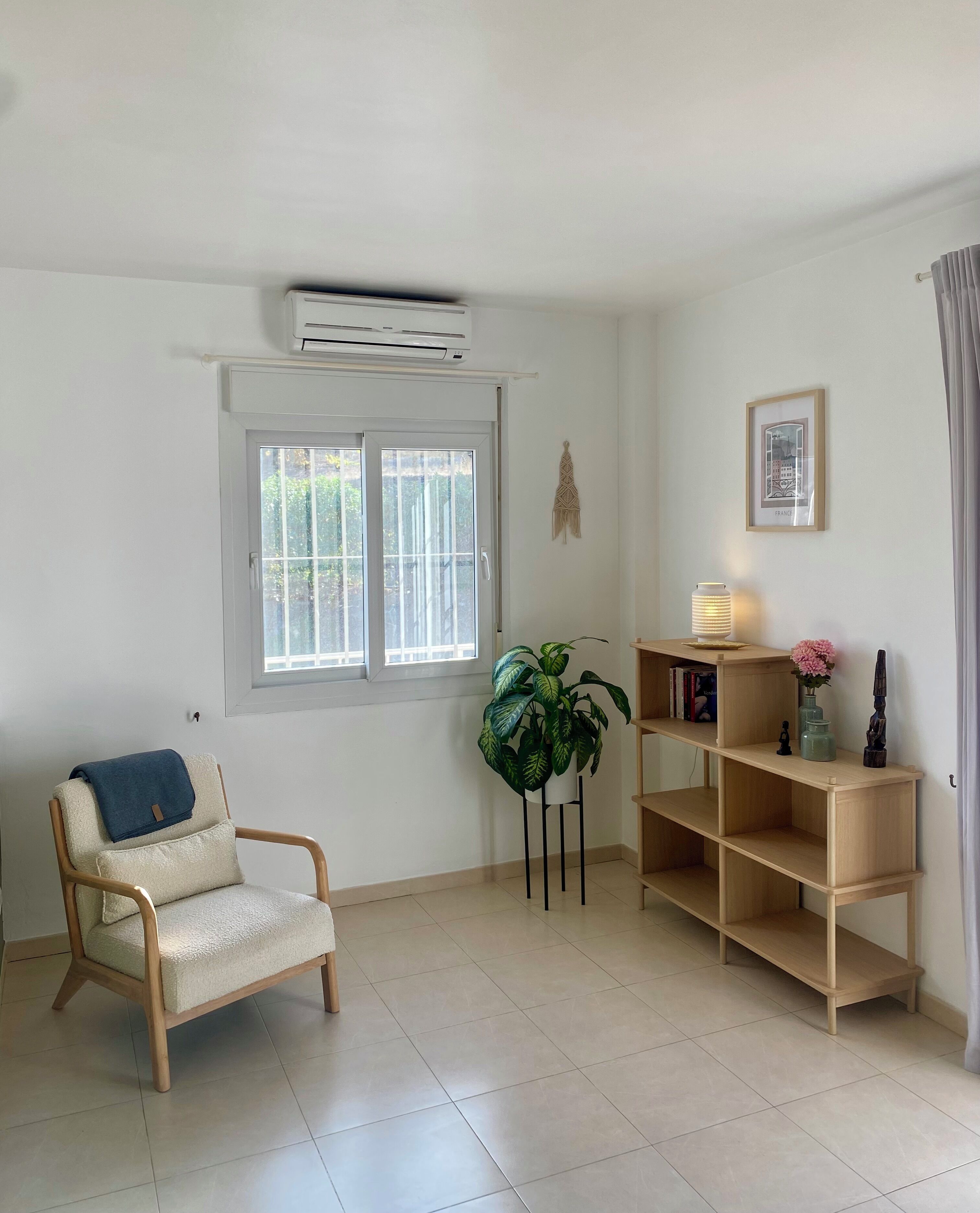 Una habitación con una silla, una planta en maceta, una estantería con libros y un cuadro colgado en la pared.