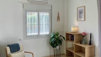Una habitación con una silla, una planta en maceta, una estantería con libros y un cuadro colgado en la pared.