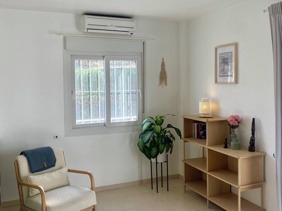 Una habitación con una silla, una planta en maceta, una estantería con libros y un cuadro colgado en la pared.