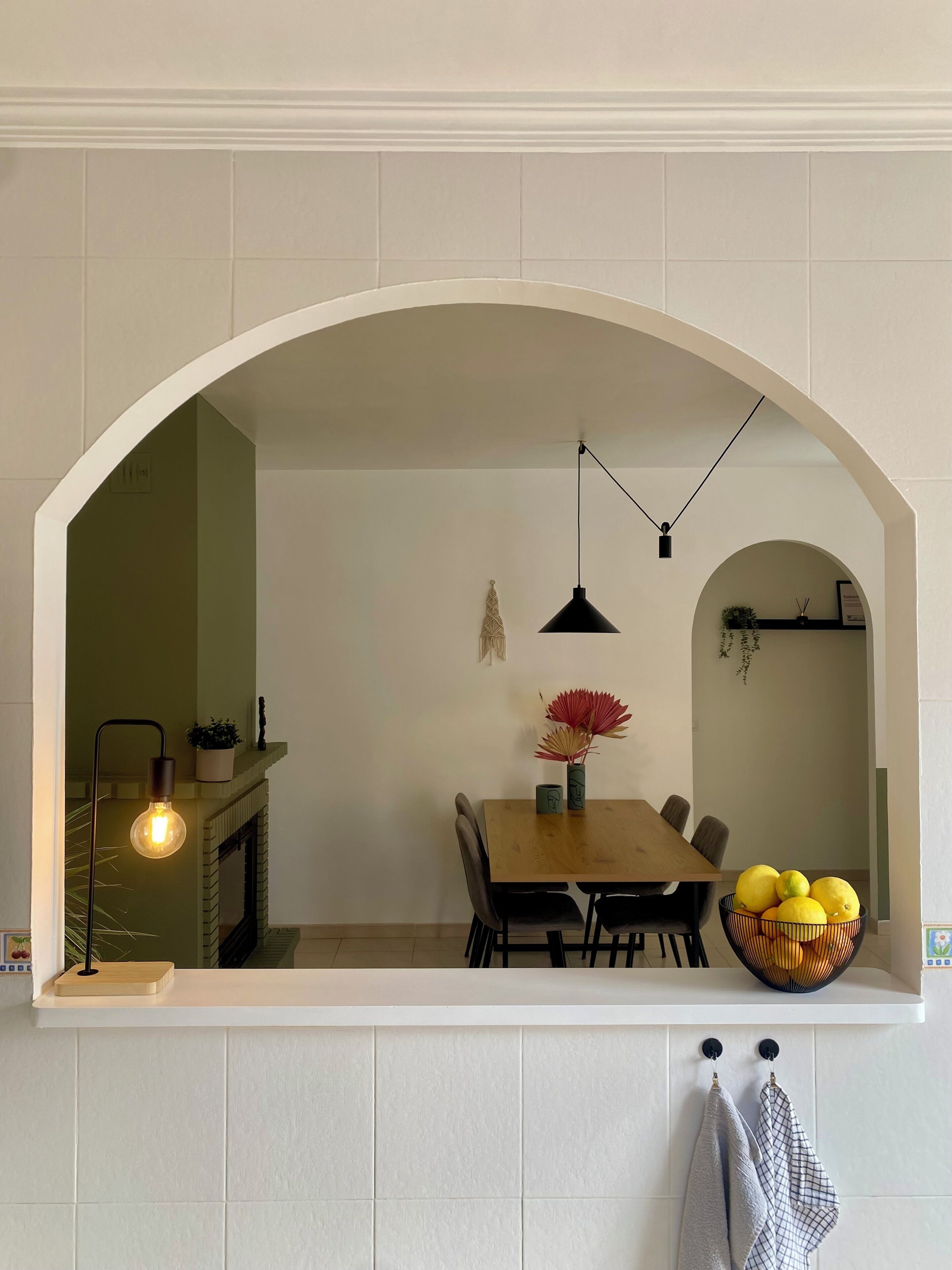 Un comedor con una mesa de madera, sillas, un jarrón con flores, un cuenco de limones y una lámpara colgante.