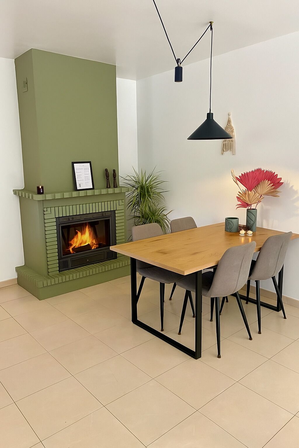 A dining area with a green fireplace, a wooden table, and four chairs.