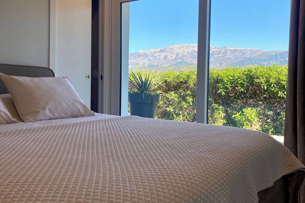 Une chambre avec un grand lit, une porte et une vue sur les montagnes par la fenêtre.