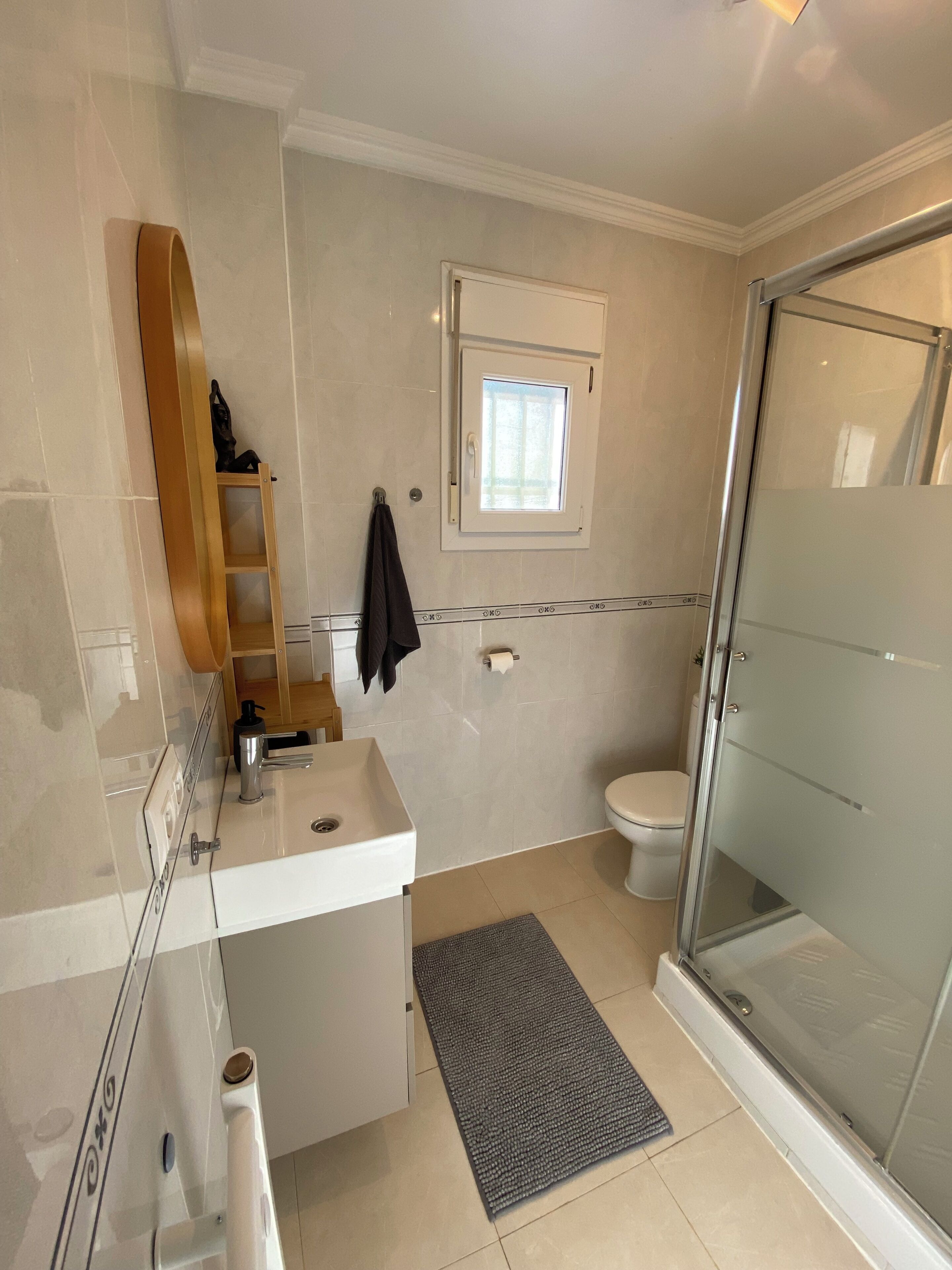 A bathroom with a shower, toilet, sink, and a window.