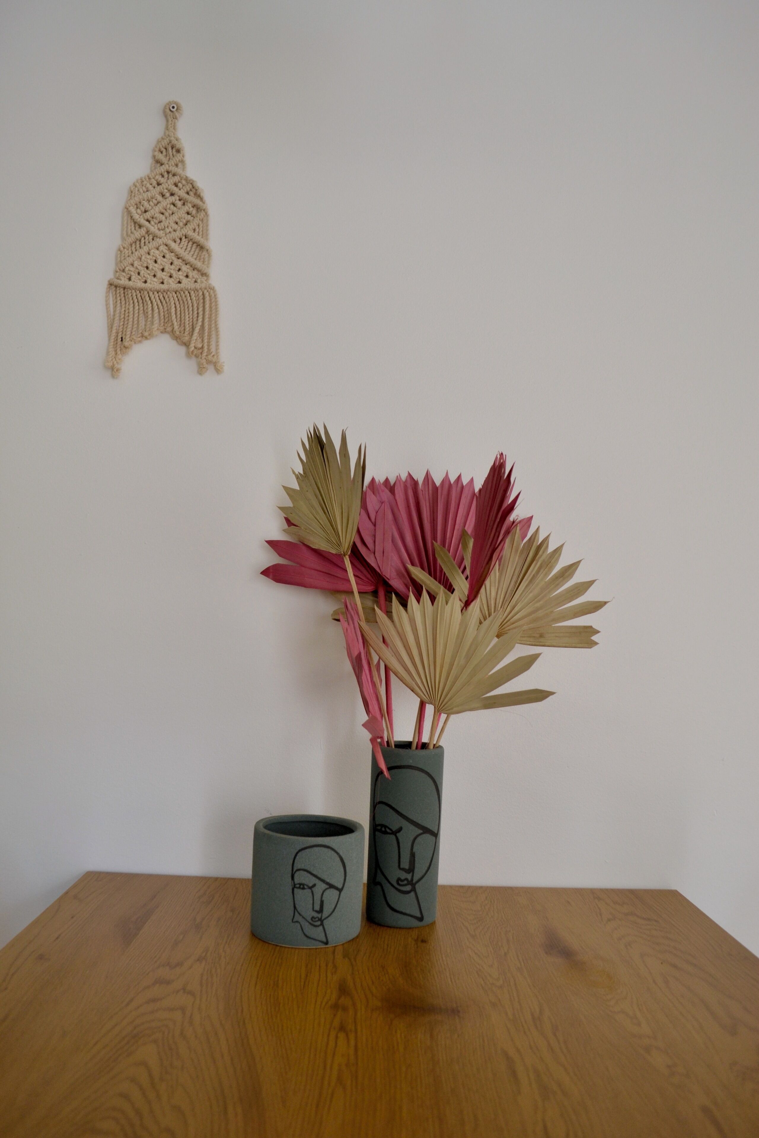 A wooden table with two ceramic vases containing decorative paper fans and a macramé wall hanging.