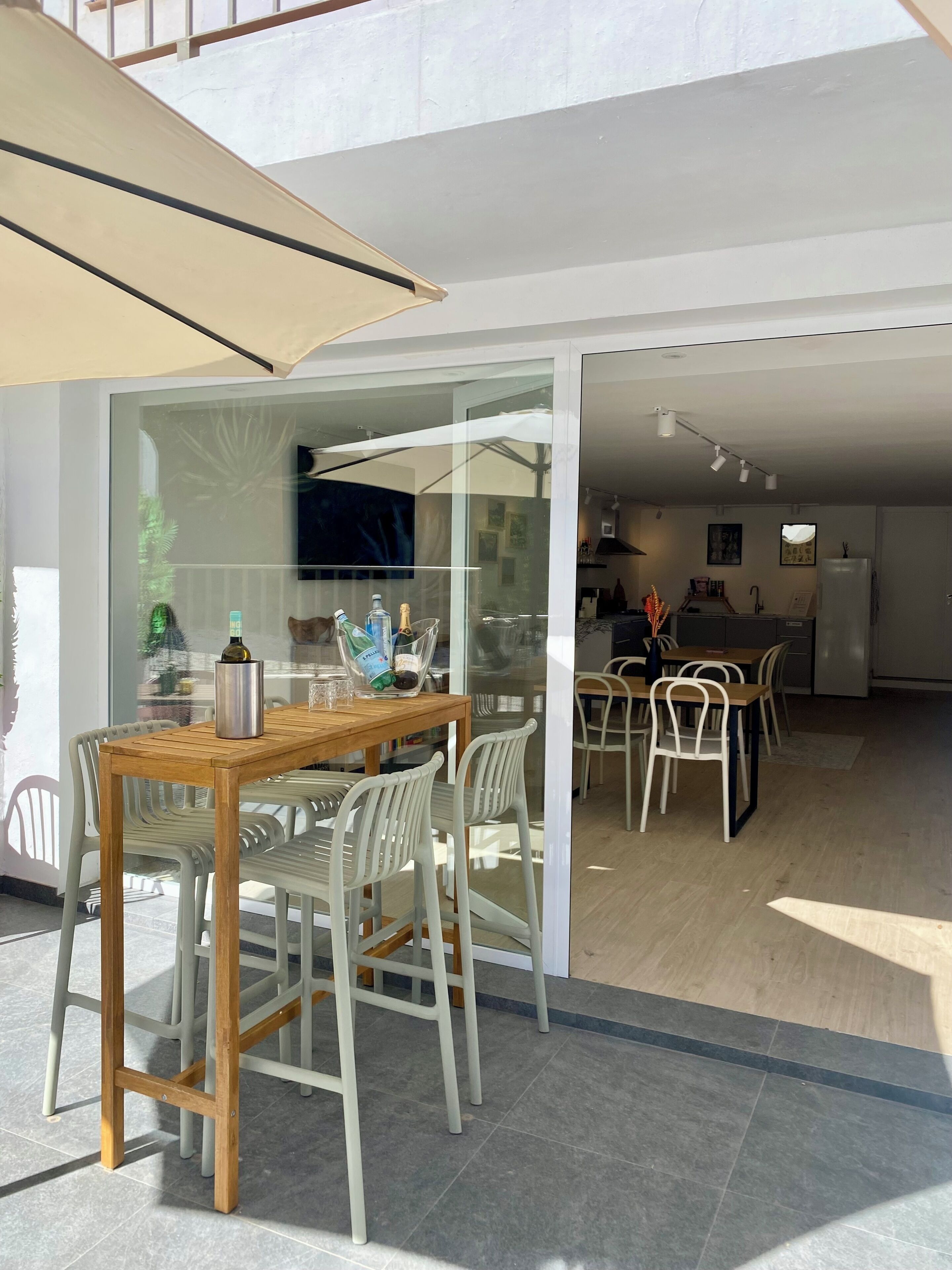 Una zona de menjador moderna amb taula i cadires de fusta, un separador de vidre i una cuina al fons.