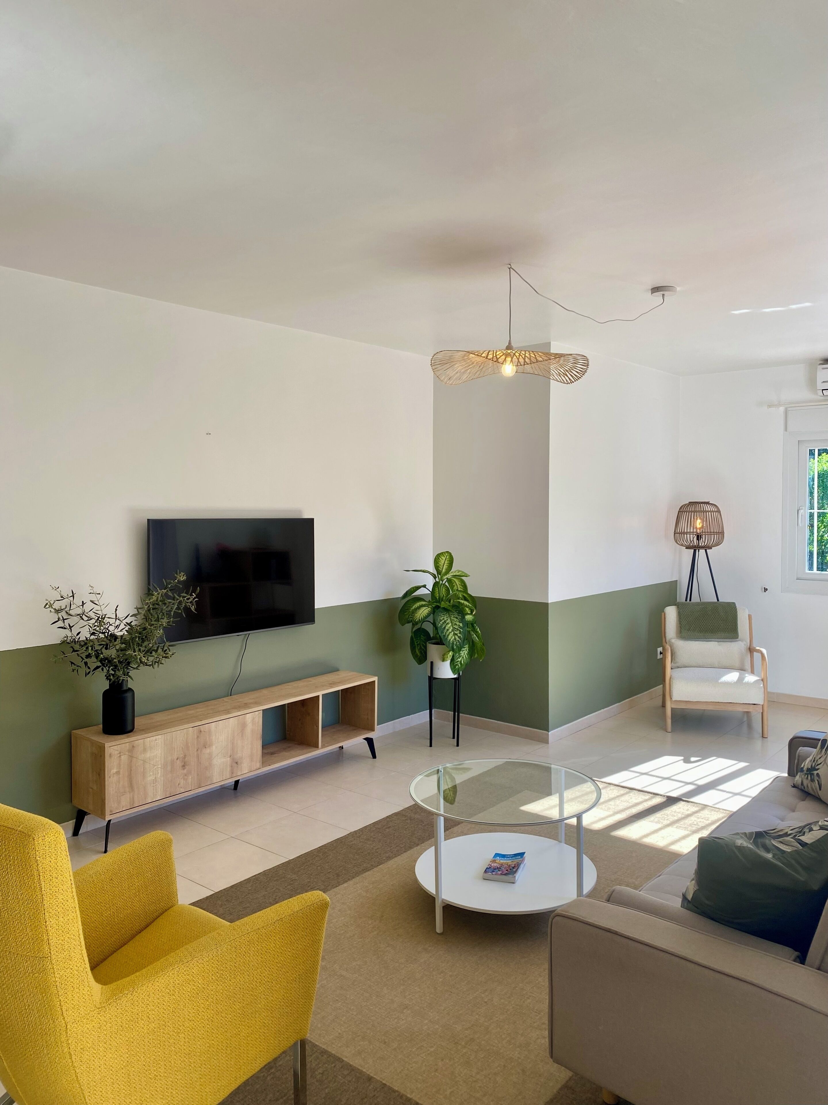 A living room with a TV, sofa, yellow chair, round coffee table, and a potted plant.