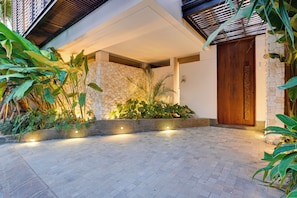 Une entrée moderne, avec un mur en pierre, une porte en bois et une zone pavée agrémentée de plantes.