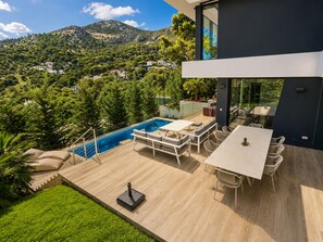 Una casa moderna con piscina, mobiliario exterior y vistas a una zona montañosa.