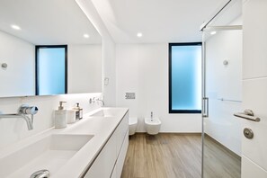 Un baño moderno con un espejo grande, una bañera, un inodoro y un bidé.