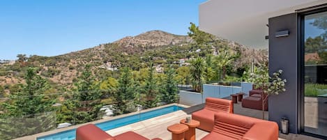 A modern outdoor pool area with seating and a view of a mountainous landscape.