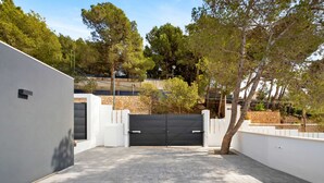 A paved driveway leading to a gated entrance, surrounded by white walls and trees. - Villa Pinares de San Antón Sea, City & Mountain Views (Málaga)