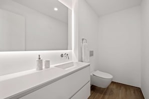 A modern bathroom with a white vanity, a large mirror, a toilet, and a towel rack.