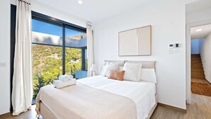 A bedroom with a large window, a bed with white linens, a bedside table, and a framed picture on the wall. - Villa Pinares de San Antón Sea, City & Mountain Views (Málaga)
