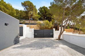 A paved driveway leading to a gated entrance, surrounded by white walls and trees.