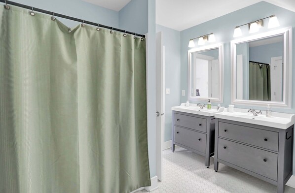 A bathroom with a shower curtain, two sinks, and a vanity with drawers.
