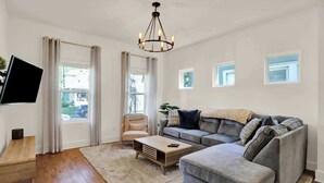 A living room with a grey sofa, a wooden coffee table, a beige armchair, and a TV mounted on the wall.