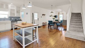 A spacious kitchen with wooden flooring, white cabinets, and pendant lighting.