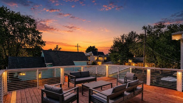 A wooden deck with outdoor furniture, a pool, and a sunset view.