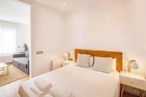 A hotel room with a large bed, two bedside tables with lamps, a grey sofa, a small table, and a radiator.