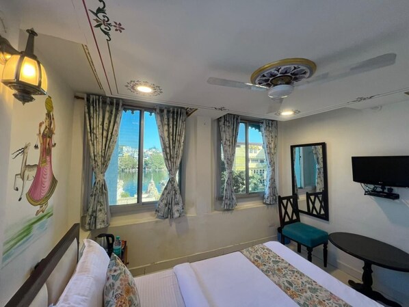 A hotel room with a bed, a desk, a chair, a television, and large windows with curtains.