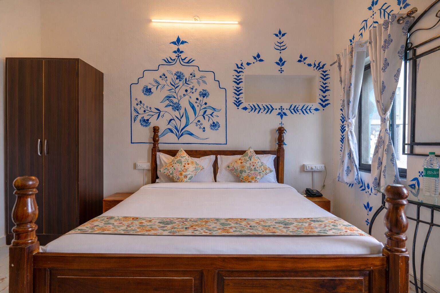 A bedroom with a wooden bed, floral bedspread, and blue floral wall art.