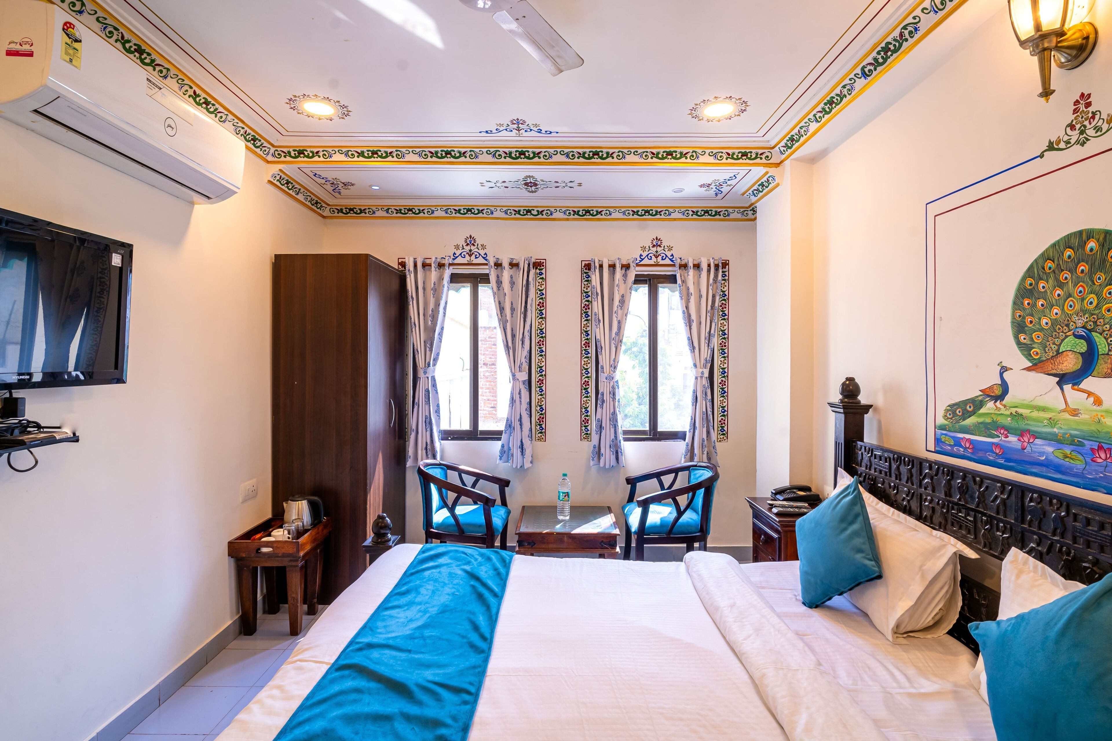 A hotel room with a large bed, two chairs, a small table, a TV, and a painting on the wall.