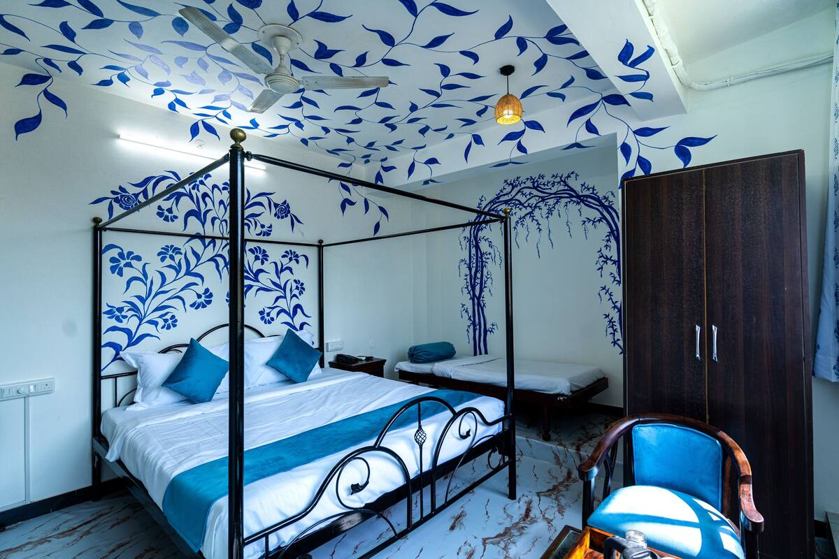 Una cama con dosel con ropa de cama azul y blanca, un armario de madera y una silla con cojín azul.