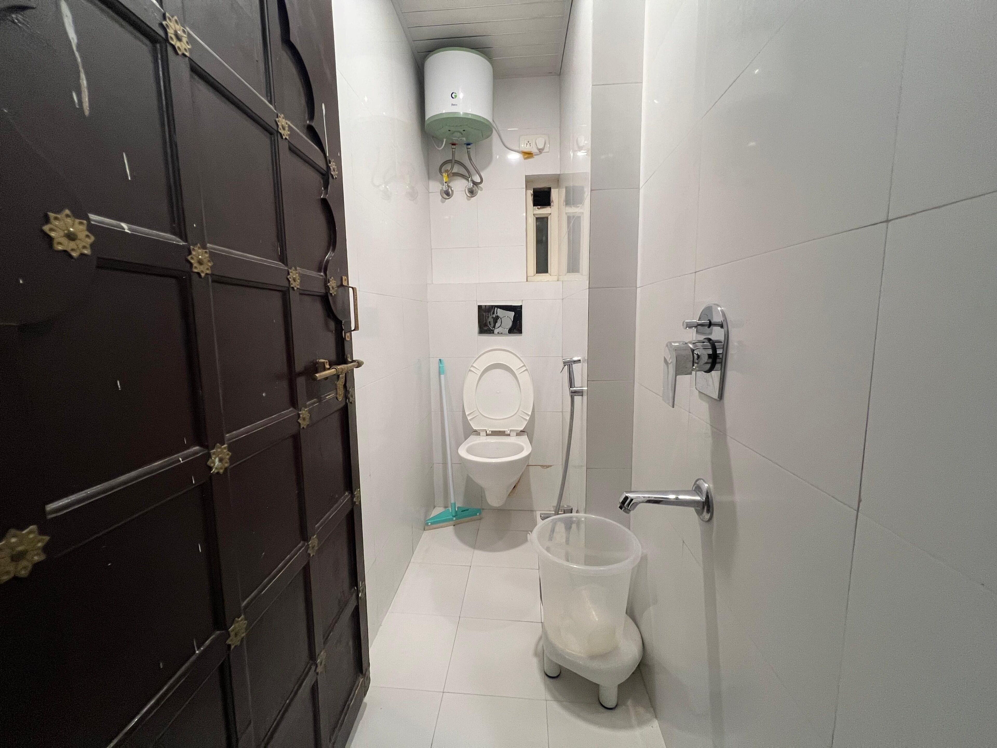A small bathroom with a toilet, a hand dryer, a trash bin, and a water heater on the wall.
