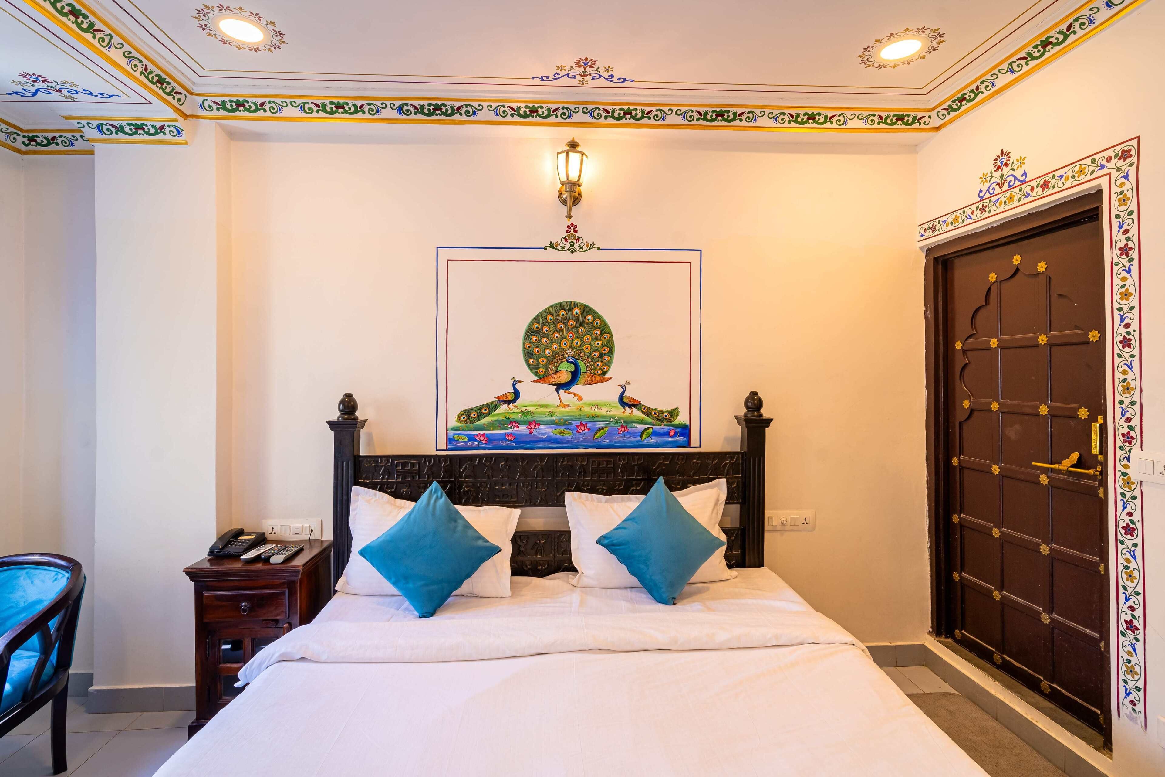 Habitación de hotel con cama, mesita de noche, teléfono, lámpara de pared y puerta con paneles decorativos.
