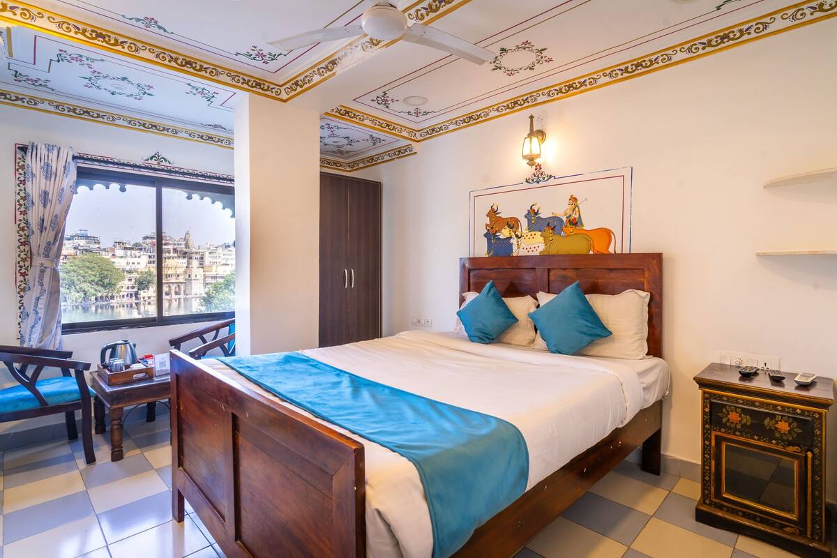 Habitación de hotel con cama, escritorio, silla, mesita de noche y ventana con vista a edificios.