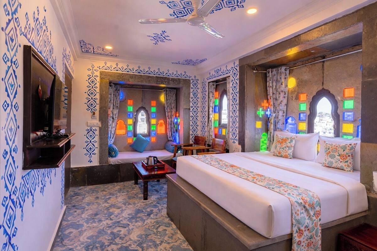 Una habitación de hotel con cama, sofá, televisor y ventana con vidrieras de colores.