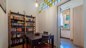 A dining area with a wooden table and chairs, a bookshelf filled with books, and a window with a view of the outside.