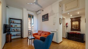A living room with a blue armchair, a bookshelf, a fireplace, and a ceiling fan.