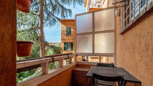 A balcony with a table and chairs, a wicker basket, and a view of trees and buildings.