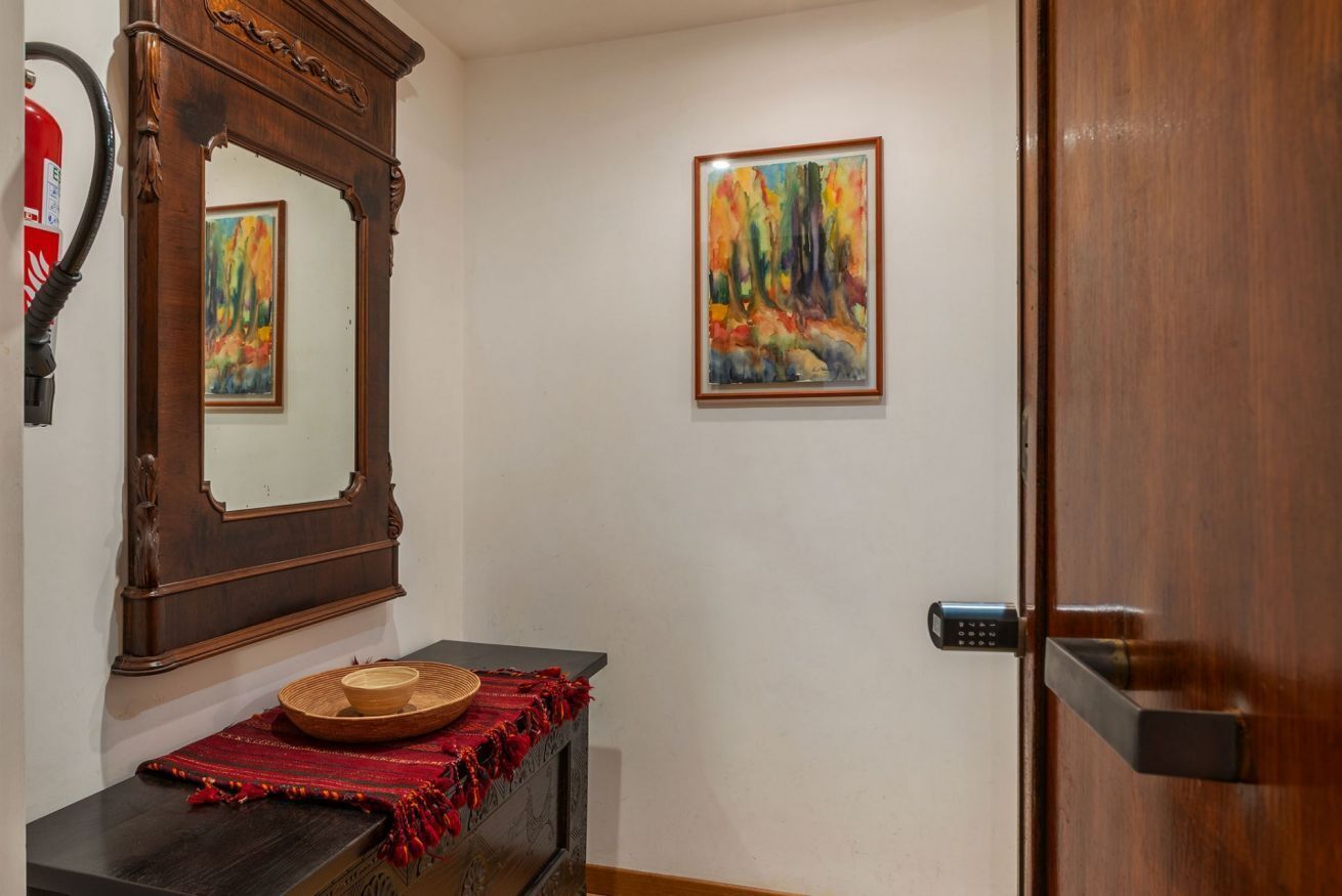 A hallway with a wooden door, a mirror, a painting, and a small table with a woven basket.