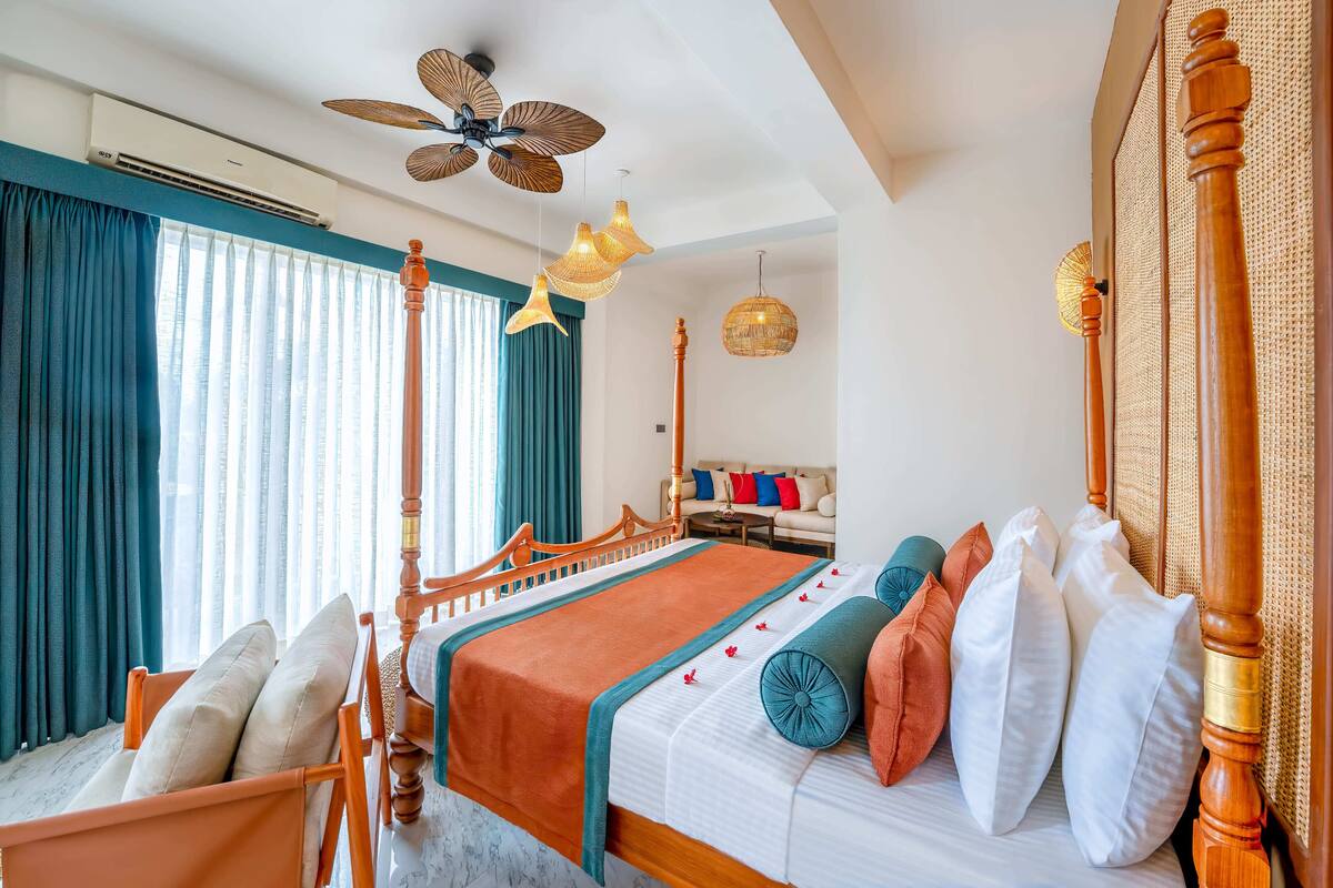 A well-lit bedroom with a four-poster bed, a ceiling fan, and a view of a balcony.