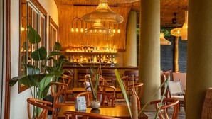 A restaurant with wooden furniture, a bar with bottles, and hanging wicker lamps. - Chaarya Lake  (Yala)