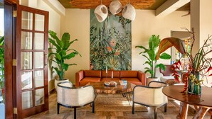 A living room with a wooden coffee table, two wicker chairs, a brown sofa, and a large abstract painting on the wall. - Chaarya Lake  (Yala)
