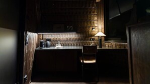 Una cocina tenuemente iluminada con paneles de madera, una encimera con una cafetera, una silla y un estante fijado a la pared.