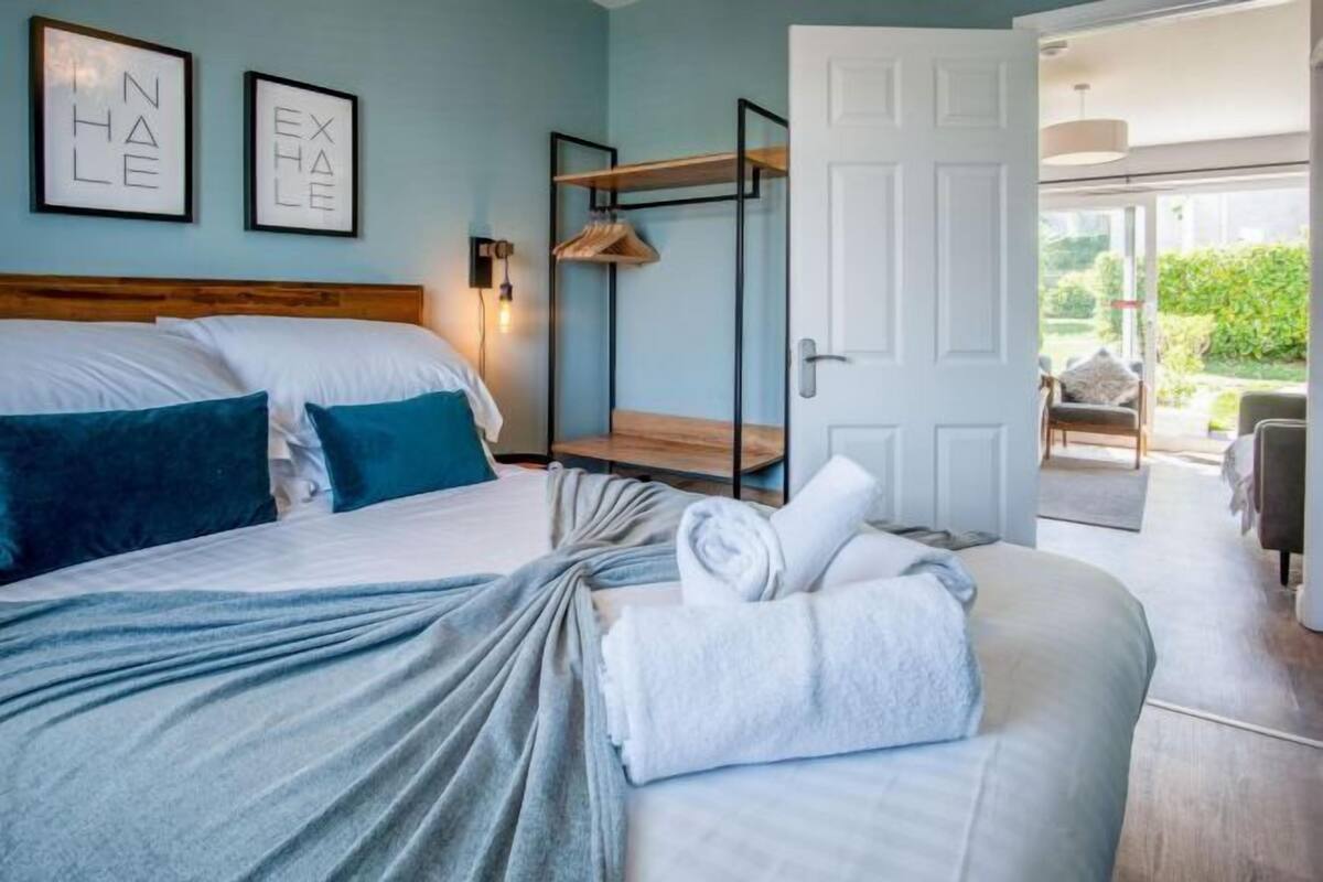 Un dormitorio con cama, un banco, una lámpara fijada en la pared y una puerta que da a un espacio exterior.