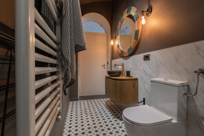Une salle de bain moderne avec des toilettes blanches, un meuble-lavabo en bois, un grand miroir et un carrelage au motif original.