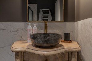 A bathroom vanity with a large stone basin, a gold-colored faucet, and two bottles of hand soap. - Design in Corso Francia 1 by Wonderful Italy (Torino)