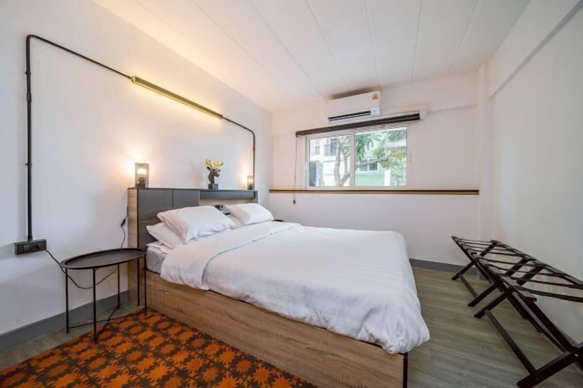 A modern bedroom with a bed, bedside table, and a window with a view of greenery.