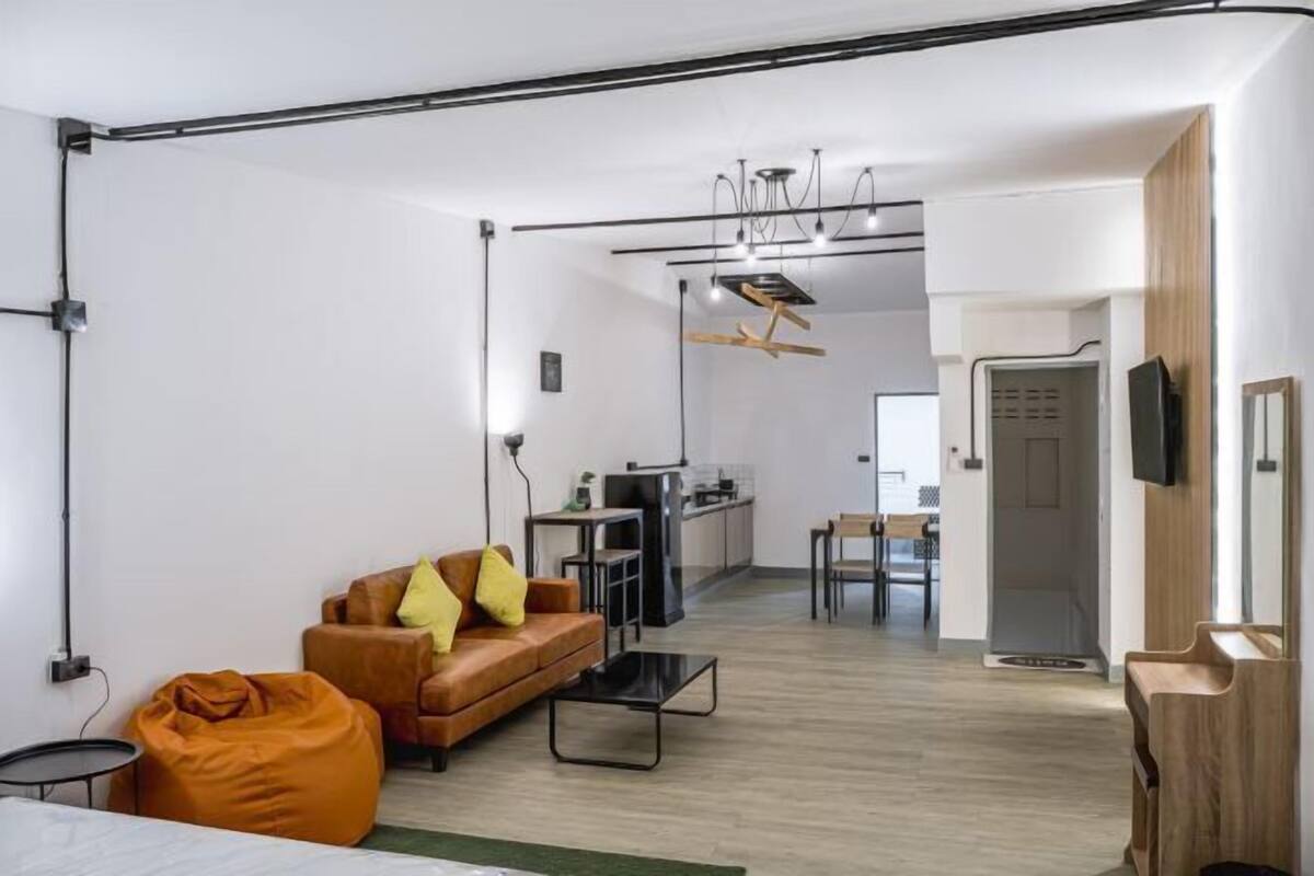 A modern living room with a sofa, coffee table, and bean bag. There is a kitchen area in the background with a dining table and chairs.