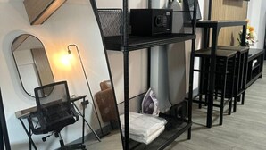 A modern room with a black metal desk, a chair, a mirror, a microwave, and a TV. - Oasis Suites - Pattaya - Huge Modern Apartments (Pattaya)