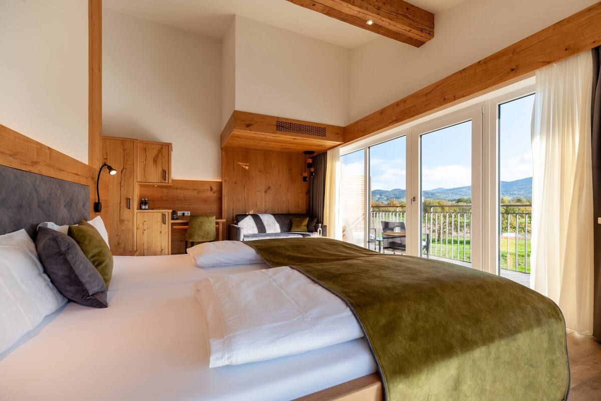 Un dormitorio con una cama grande, vigas de madera en el techo, un armario empotrado y un balcón con vistas al campo.