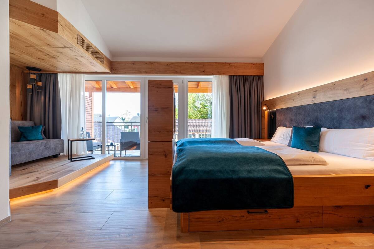 Un dormitorio moderno con cabecera de madera, una cama grande, un sofá y un balcón con vistas.