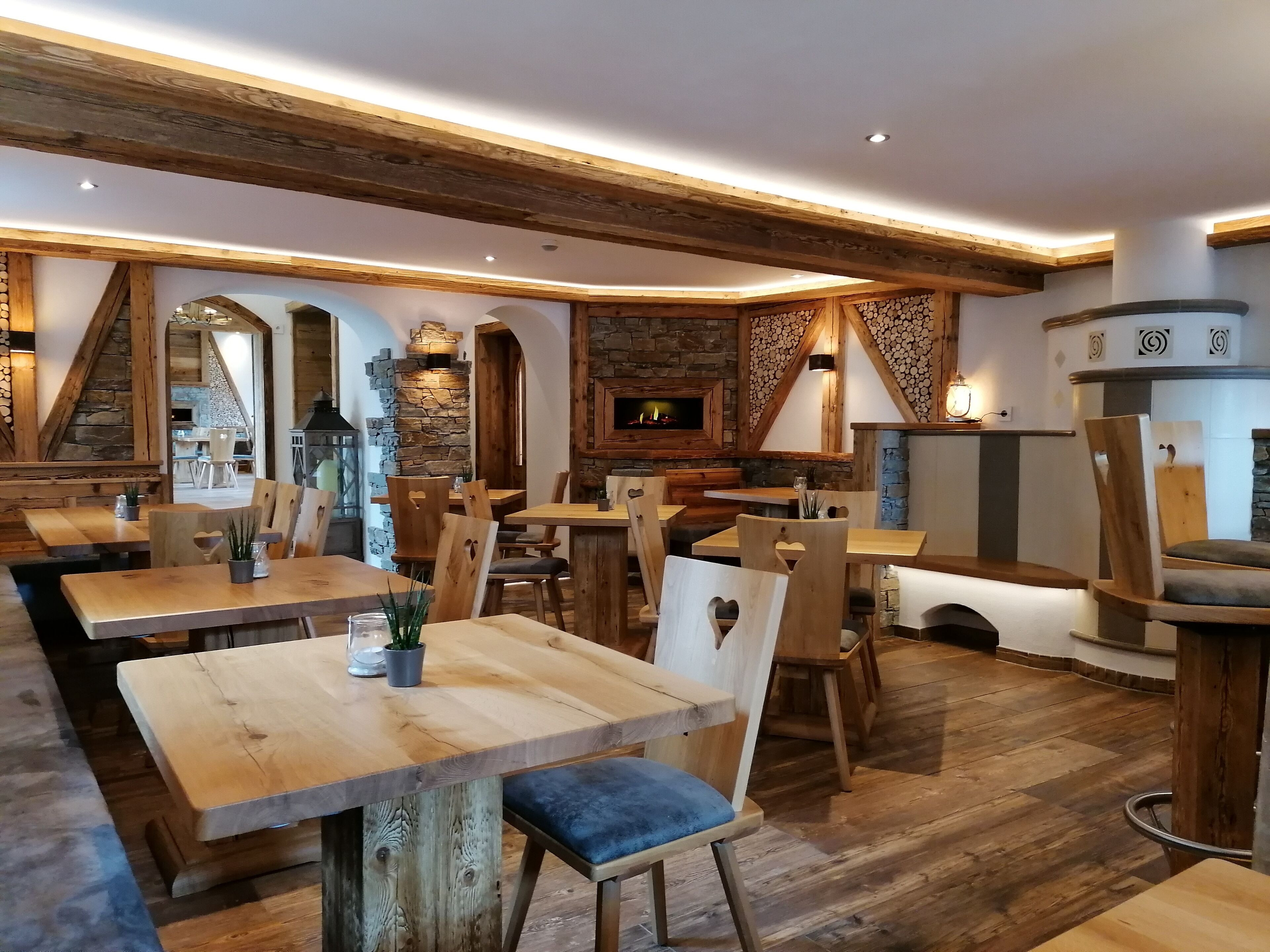 Un interior rústico con mesas y sillas de madera, paredes de piedra y una chimenea.