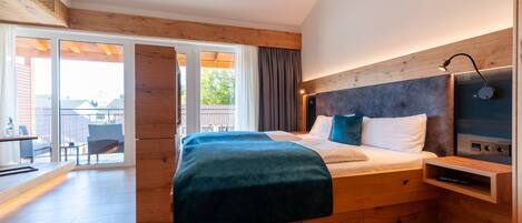 Un dormitorio moderno con cabecera de madera, una cama grande con manta azul, una mesita de noche y vistas al exterior a través de una puerta corrediza de vidrio.