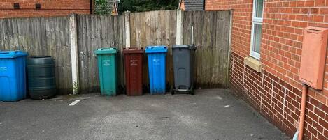 A parking area with four trash bins lined up against a wooden fence.